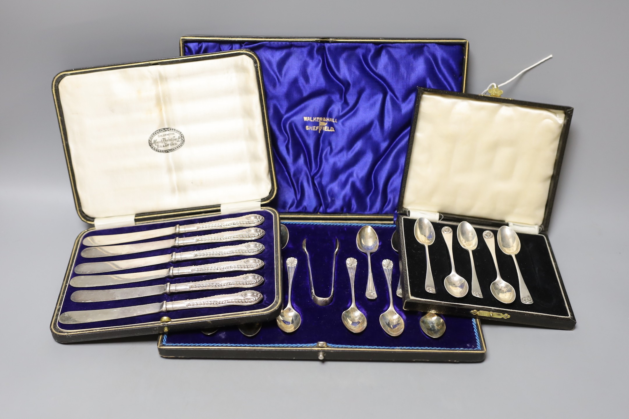 A cased set of twelve Edwardian silver teaspoons with tongs, a cased set of six tea knives and a cased set of 5 (ex 6) silver teaspoons.